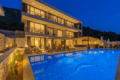 Villa Falcon Royal in Kalkan with private infinity pool, modern three-story design, luxury sun loungers, and illuminated evening ambiance surrounded by nature.