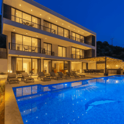 Villa Falcon Royal in Kalkan with private infinity pool, modern three-story design, luxury sun loungers, and illuminated evening ambiance surrounded by nature.