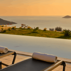 Villa Ayala infinity pool with loungers and sea view in Kalkan, surrounded by greenery and overlooking the Mediterranean islands.