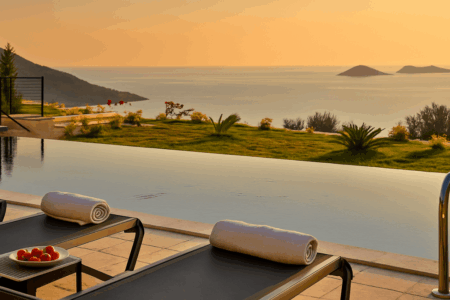 Villa Ayala infinity pool with loungers and sea view in Kalkan, surrounded by greenery and overlooking the Mediterranean islands.