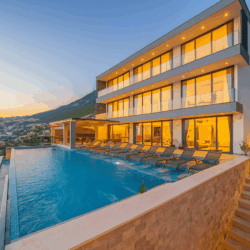 Villa Falcon Grey in Kalkan with private infinity pool, modern three-story architecture, luxury sun loungers, and panoramic sea and mountain views at sunset